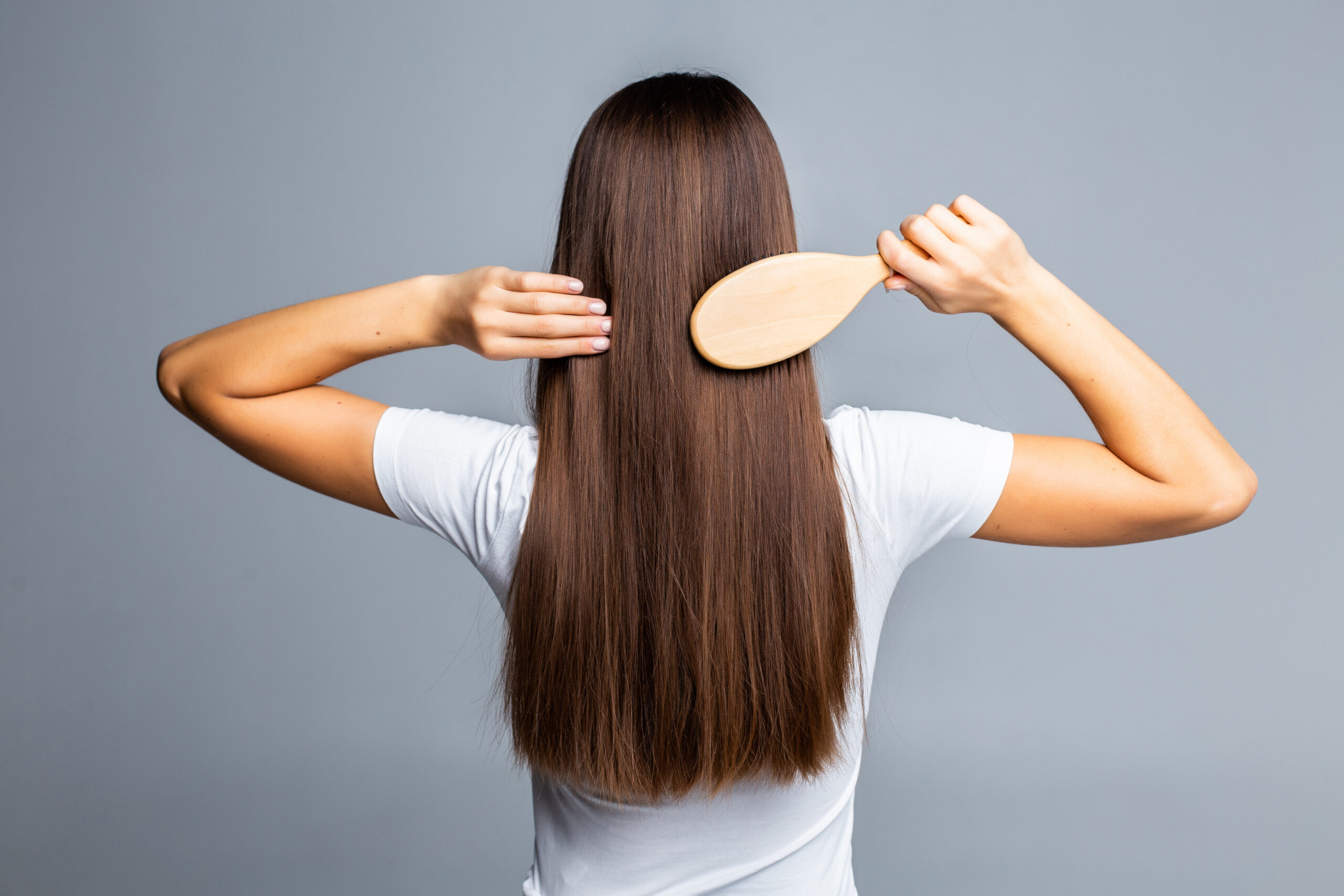 Rear view of Combing healthy long straight female hair isolated on gray background